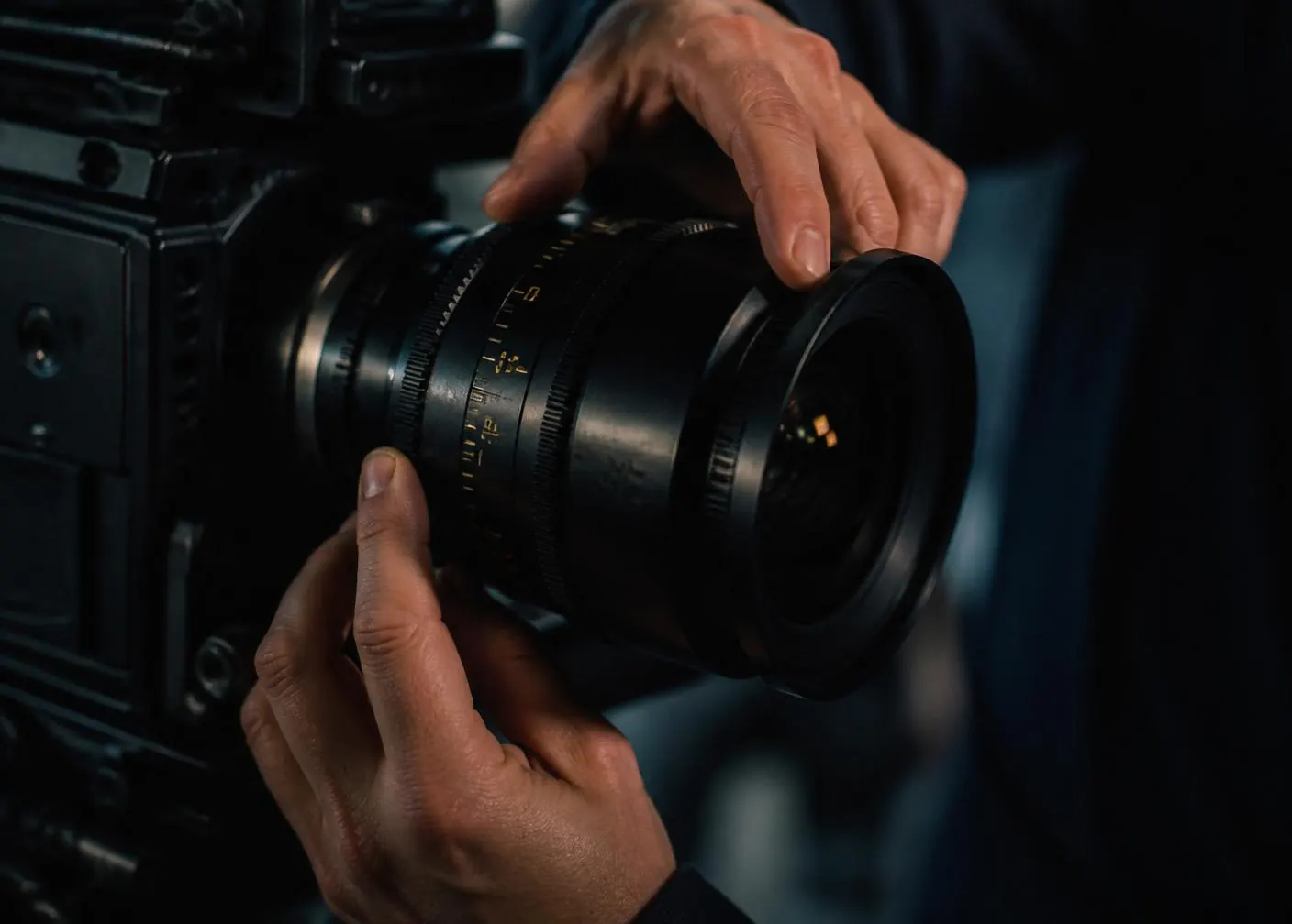 Manos de un cinematógrafo ajustando una óptica de cine sobre un cuerpo de cámara profesional
